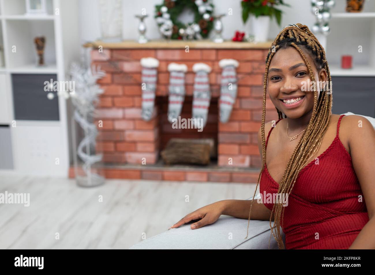 Smiling African woman sits on a sofa in a red dress. Christmas ...
