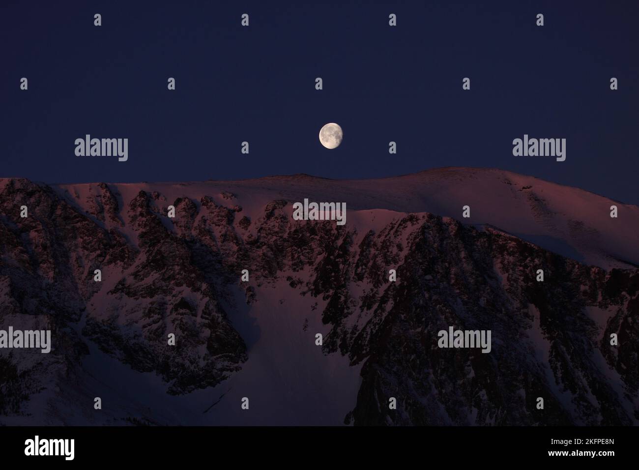 Full moon setting over snowy mountain ridge in The Sierra Nevada Mountains , California ; USA Stock Photo