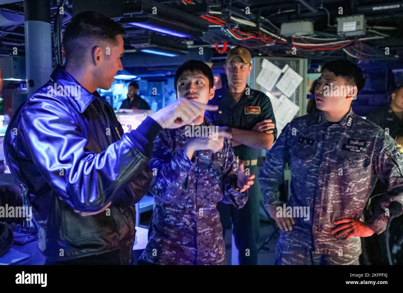 WATERS EAST OF KOREAN PENINSULA (Sept. 30, 2022) Lt. Aaron Van Driessche, left, from Simi Valley, California, Japanese Maritime Self-Defense Force sailor Lt. j. g. Ryou Kato, center left, Cmdr. Marcus Seeger, center right, commanding officer of Arleigh Burke-class guided-missile destroyer USS Benfold (DDG 65), and Republic of Korea Navy sailor Lt. Taehyung Kim, right, discuss similarities between combat systems during a trilateral anti-submarine warfare exercise in the ship’s combat information center, Sept. 30. Benfold, and Carrier Strike Group (CSG) 5, is conducting a tri-lateral anti-submar Stock Photo