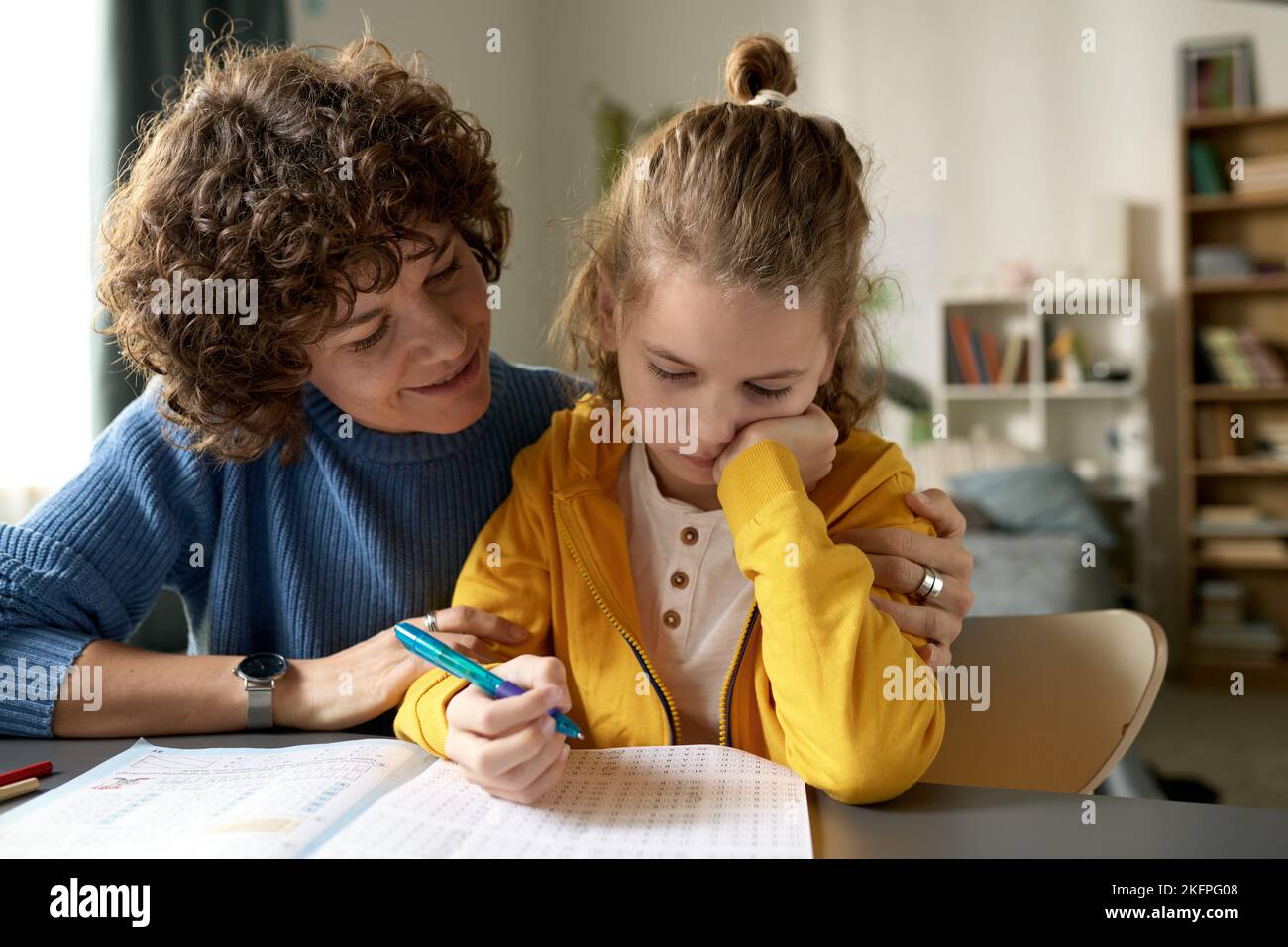Young mom helping her little son with study, they sitting at desk and trying to do homework together Stock Photo