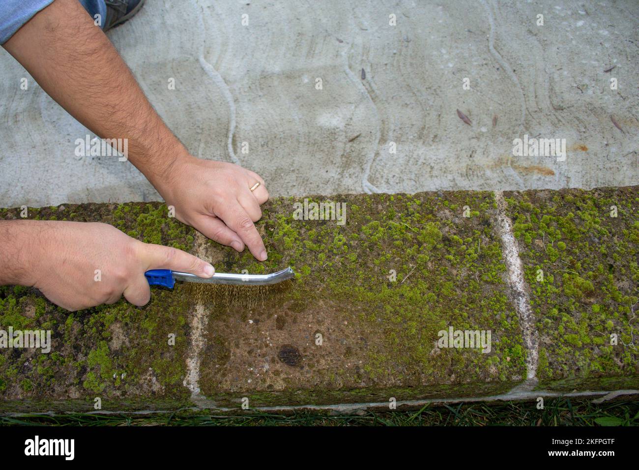 Image of the hands of a handyman using a steel brush to remove mold and moisture from bricks