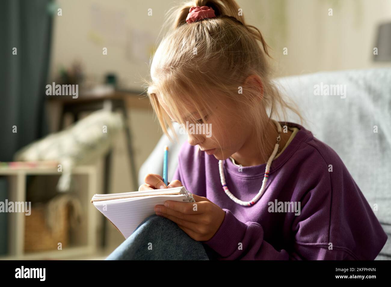 Little girl writing her secrets in her diary while sitting in the bedroom Stock Photo