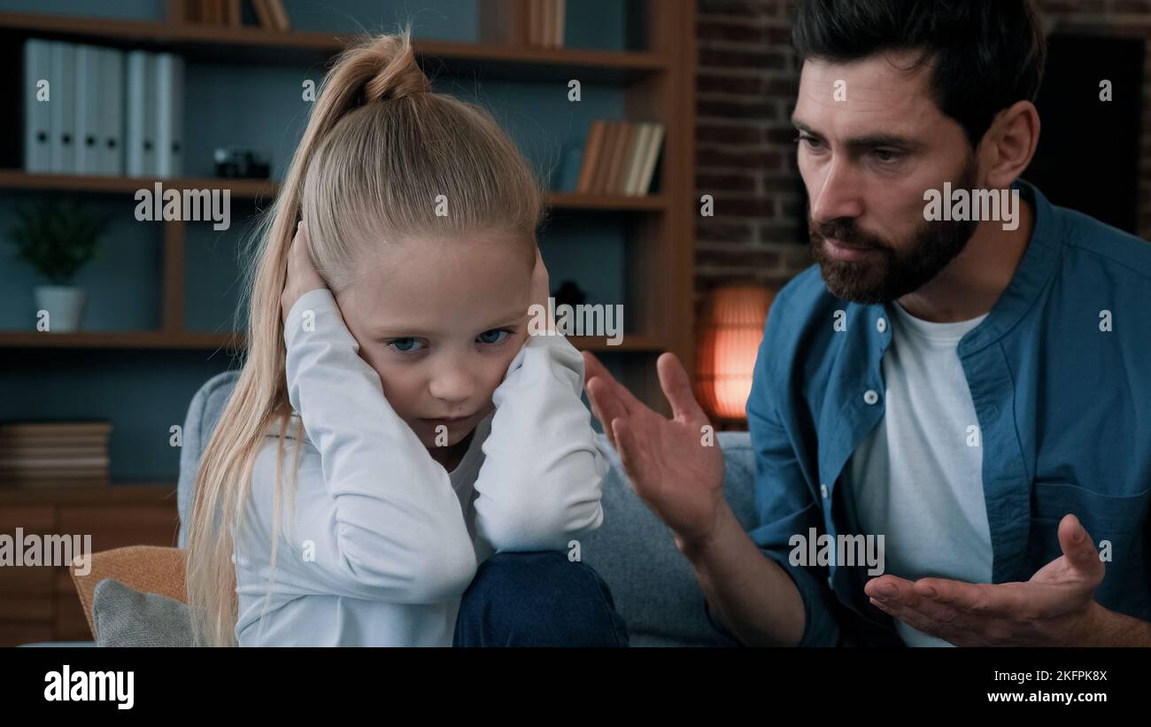 Sad offended little child daughter feel stress cover ears ignoring scream caucasian angry annoyed man dad shouting on girl for bad behavior and Stock Photo
