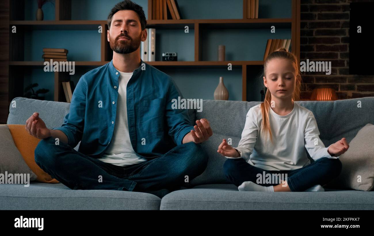 Peaceful caucasian family young father man with daughter little girl kid child sit in lotus pose meditate practice yoga together at home health Stock Photo
