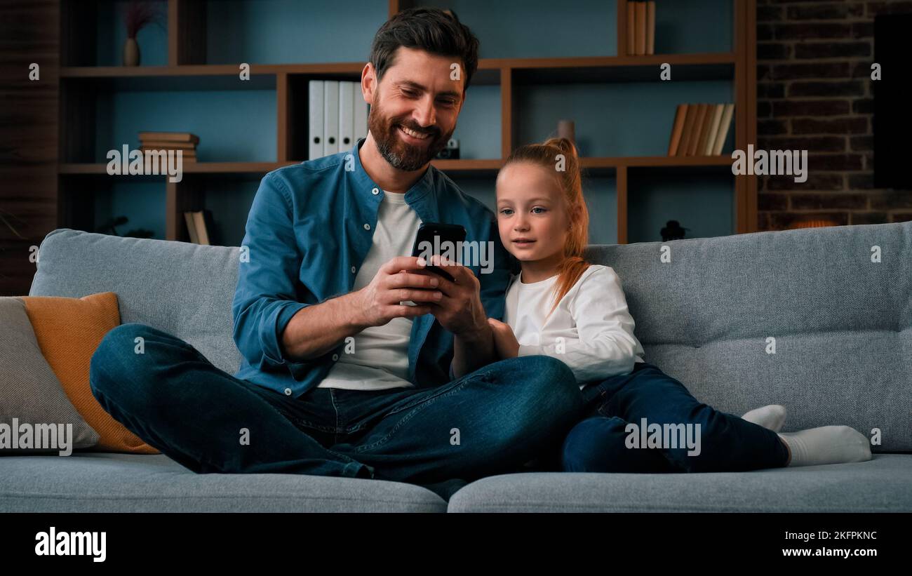 Happy family young child girl and single daddy look at modern gadget smartphone watch video online together internet communication caucasian father Stock Photo