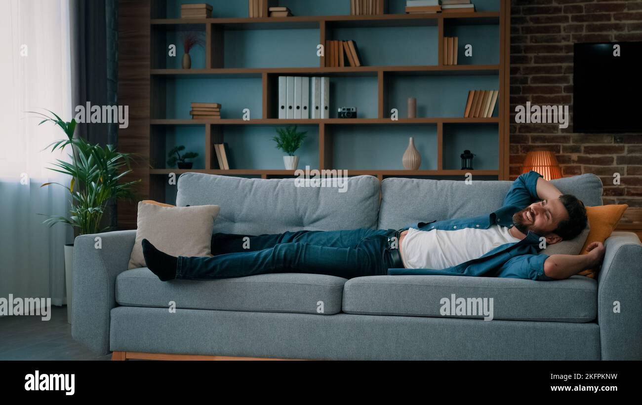 Exhausted caucasian man jumping on soft couch in living room falling down on comfortable sofa enjoy daily nap healthy rest after working day has Stock Photo