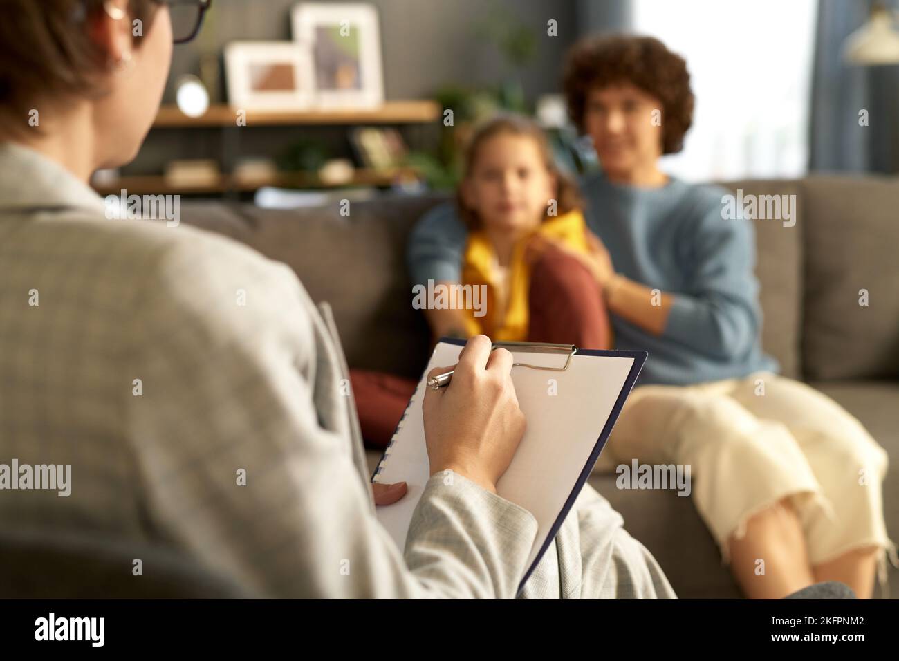 Close-up of child psychologist making notes in document while talking to mom and her son during her visit to home Stock Photo
