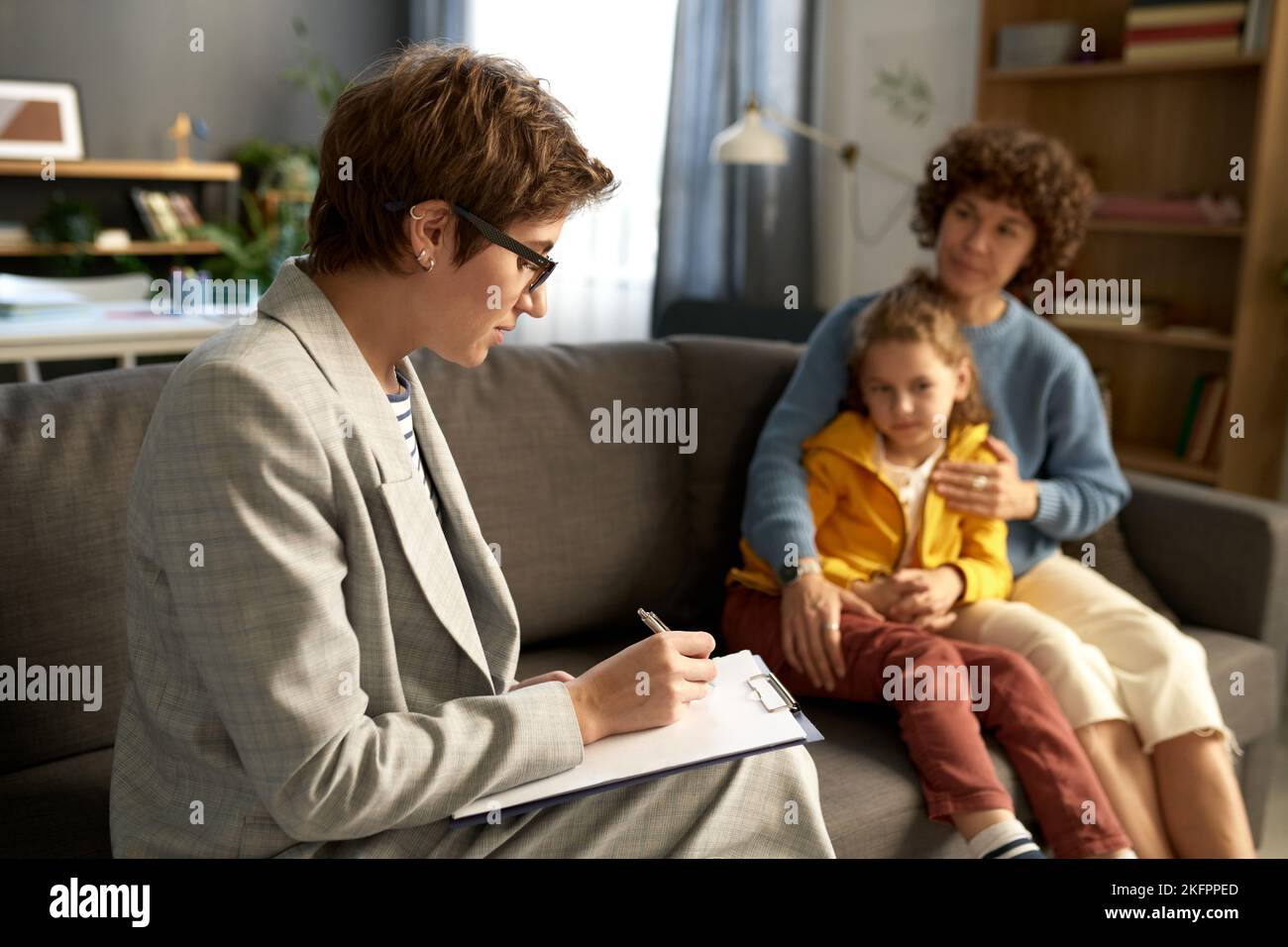 Social worker making notes in document while talking to difficult child and his mom at home Stock Photo