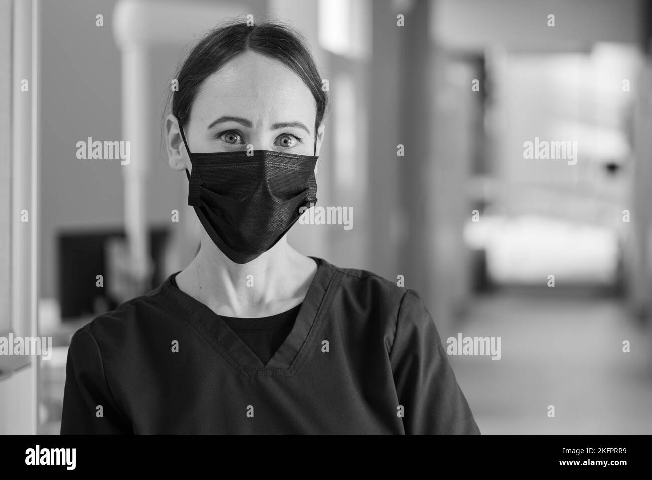 A grayscale portrait of a nurse wearing a face mask captured in the hallways of a hospital Stock Photo