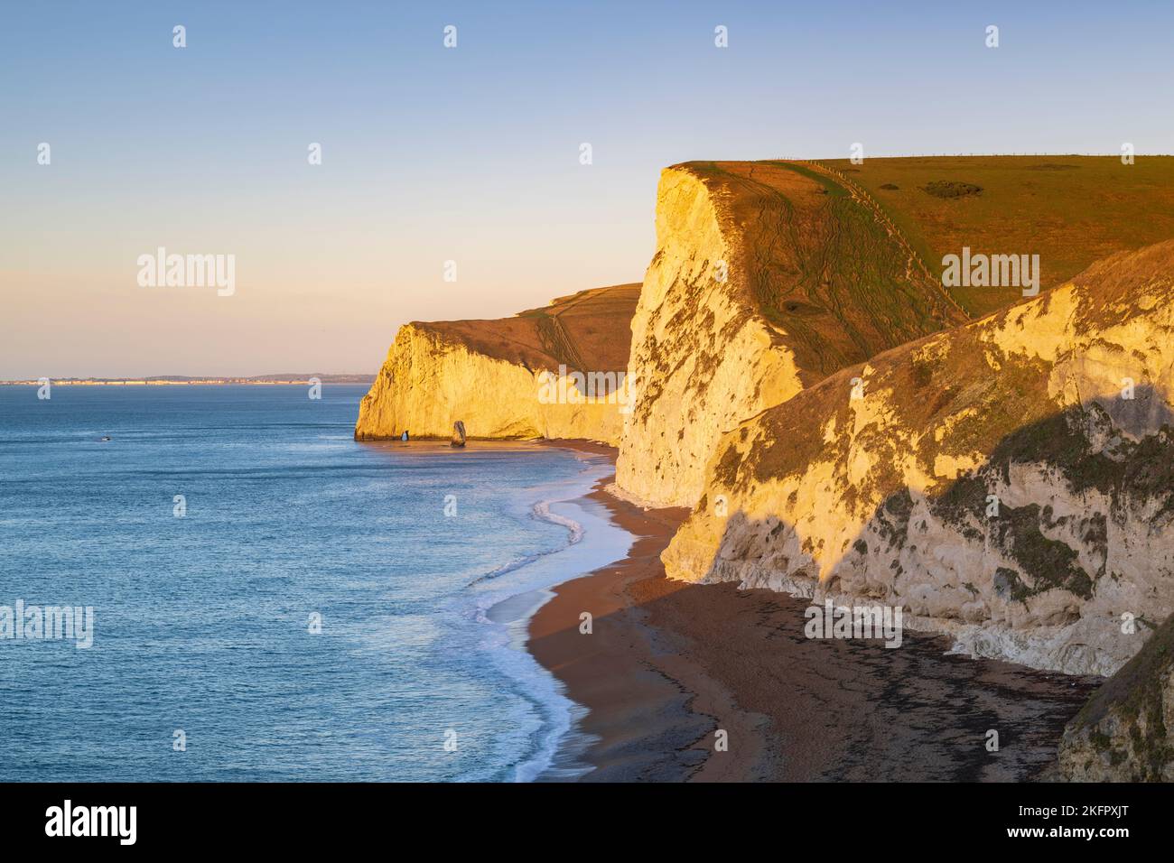 Early morning sunshine illuminates the chalk cliffs at Swyre Head and Bats Head at Durdle Door on the Dorset Jurassic Coast on a cold, clear morning. Stock Photo