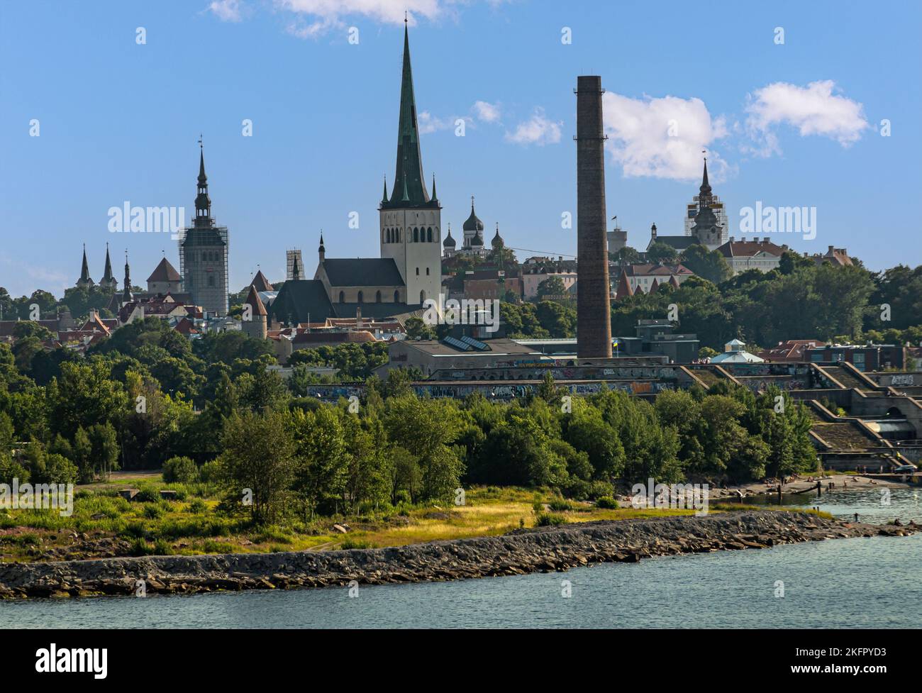 Estonia, Tallinn - July 21, 2022: Cityscape showing the towers of old town: churches, rampart lookouts, and a historic lone chimney in front under blu Stock Photo