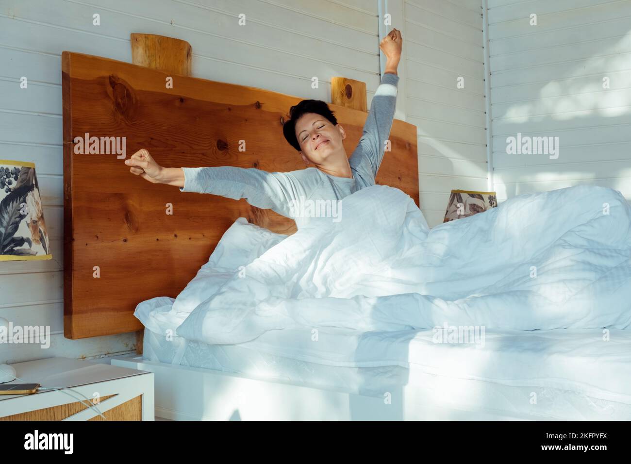 Smiling pretty cute female sitting on comfort bed and stretching in