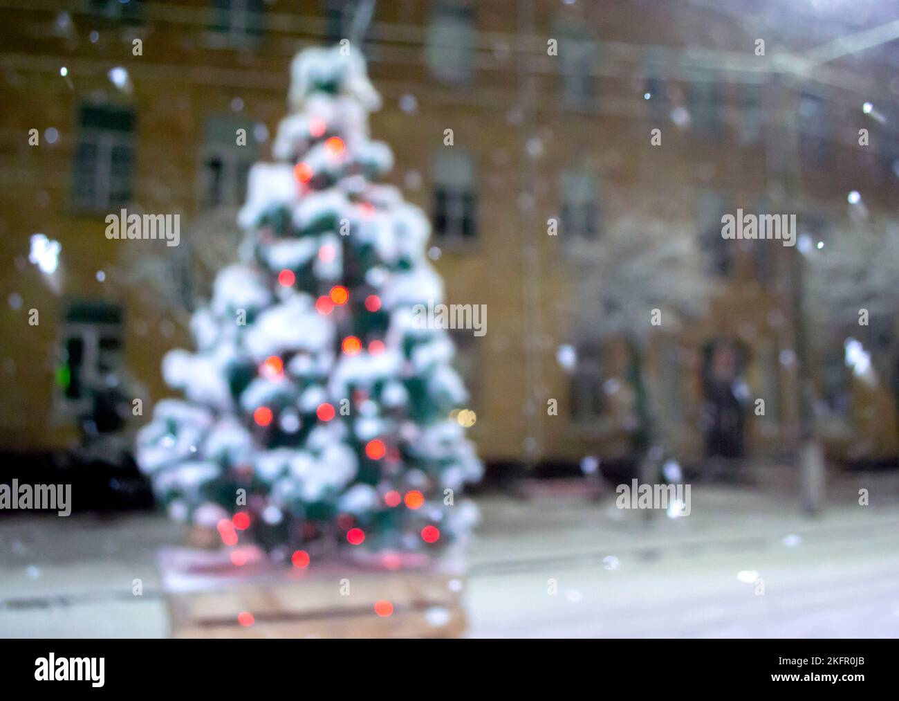 Christmas tree covered snow, glowing colorful lights during snowfall outdoors. Abstract Christmas New Year background. Blurred snowy winter background. Light twinkling. Stock Photo