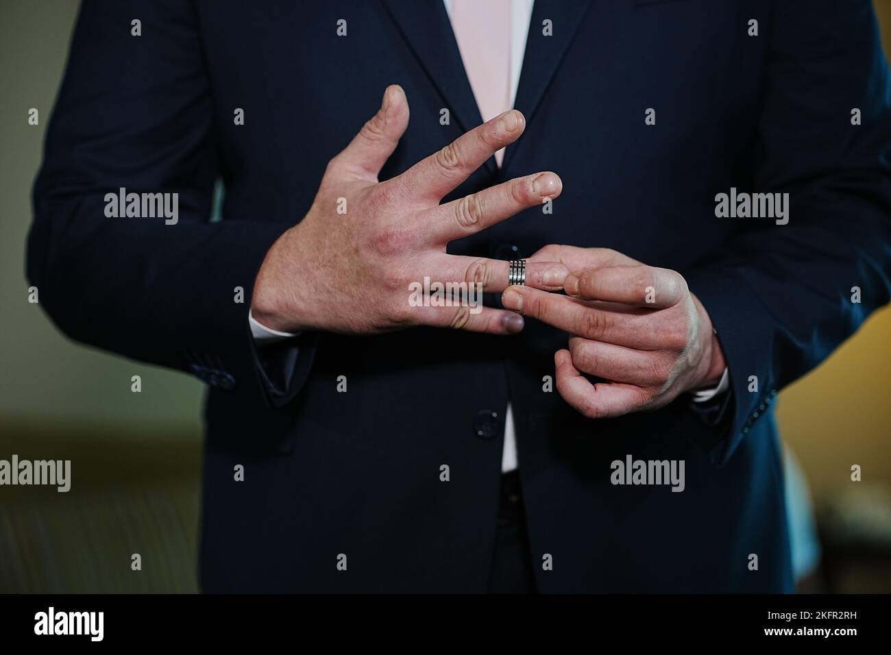 A closeup shot of a groom in a suit putting on his ring at his wedding ...