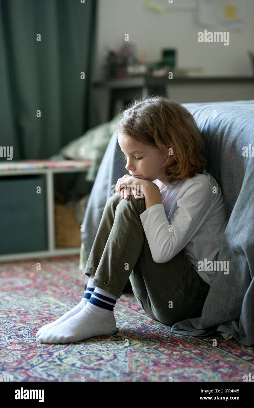 Sad little boy sitting on floor in bedroom and experiencing his fears or emotions Stock Photo