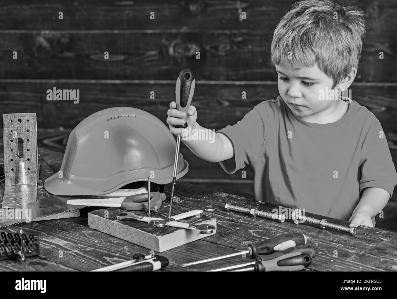 Concentrated kid binding screws to wooden board. Blond boy playing with tools set. Preschooler learning new skills Stock Photo