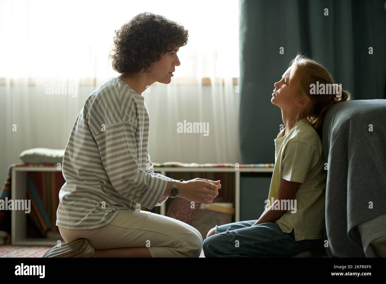 Young mother having conversation with her difficult daughter while they sitting in the room Stock Photo