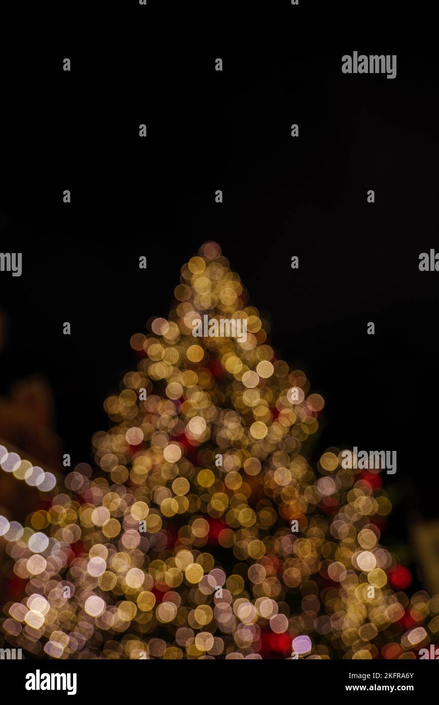 Blurry Gold and red bokeh of Christmas light on Christmas tree on black background. Colourful Glitter bokeh from blurry decoration bulbs. Stock Photo