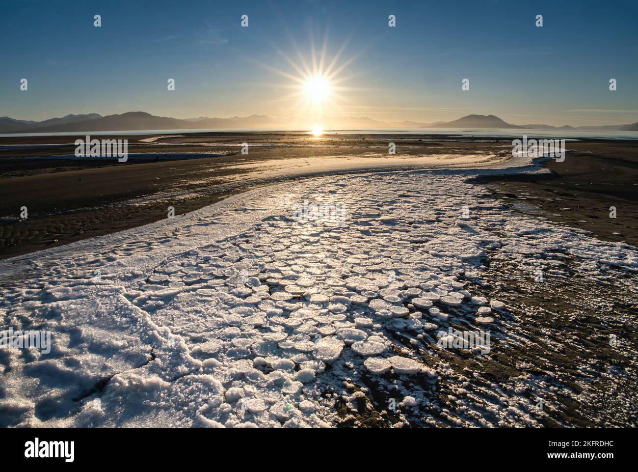 Ice circles stranded on beach at low tide with setting sunburst on a sunny winter day in Southeast Alaska. Stock Photo