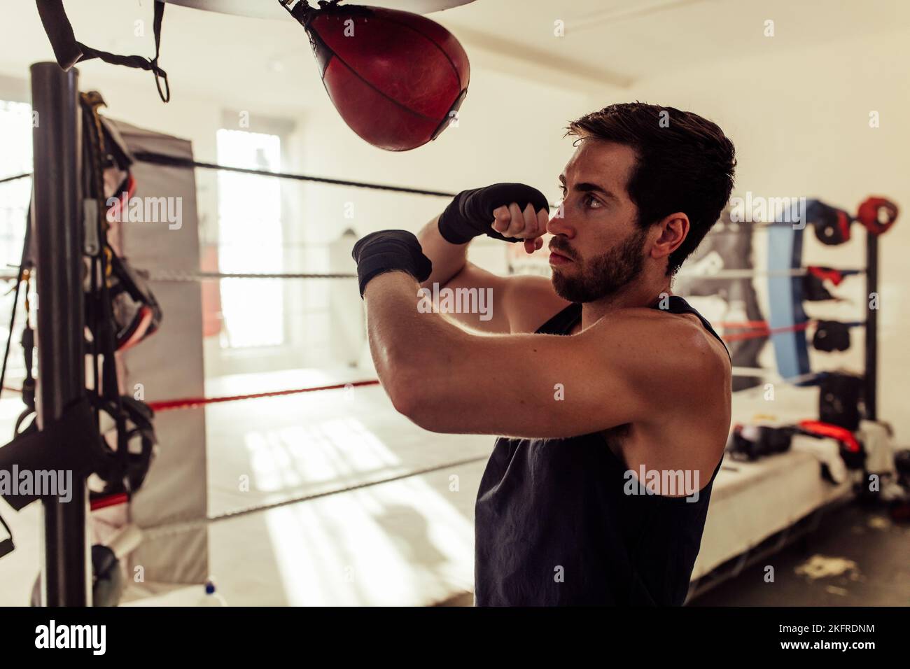 Boxer with a beard striking a punching bag in a fitness gym. Athletic young man working out in a boxing gym. Stock Photo