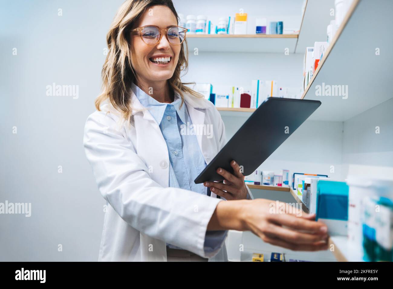 Happy pharmacist getting medication from a shelf in a chemist. Female healthcare worker filling prescriptions using a tablet. Woman working in a pharm Stock Photo