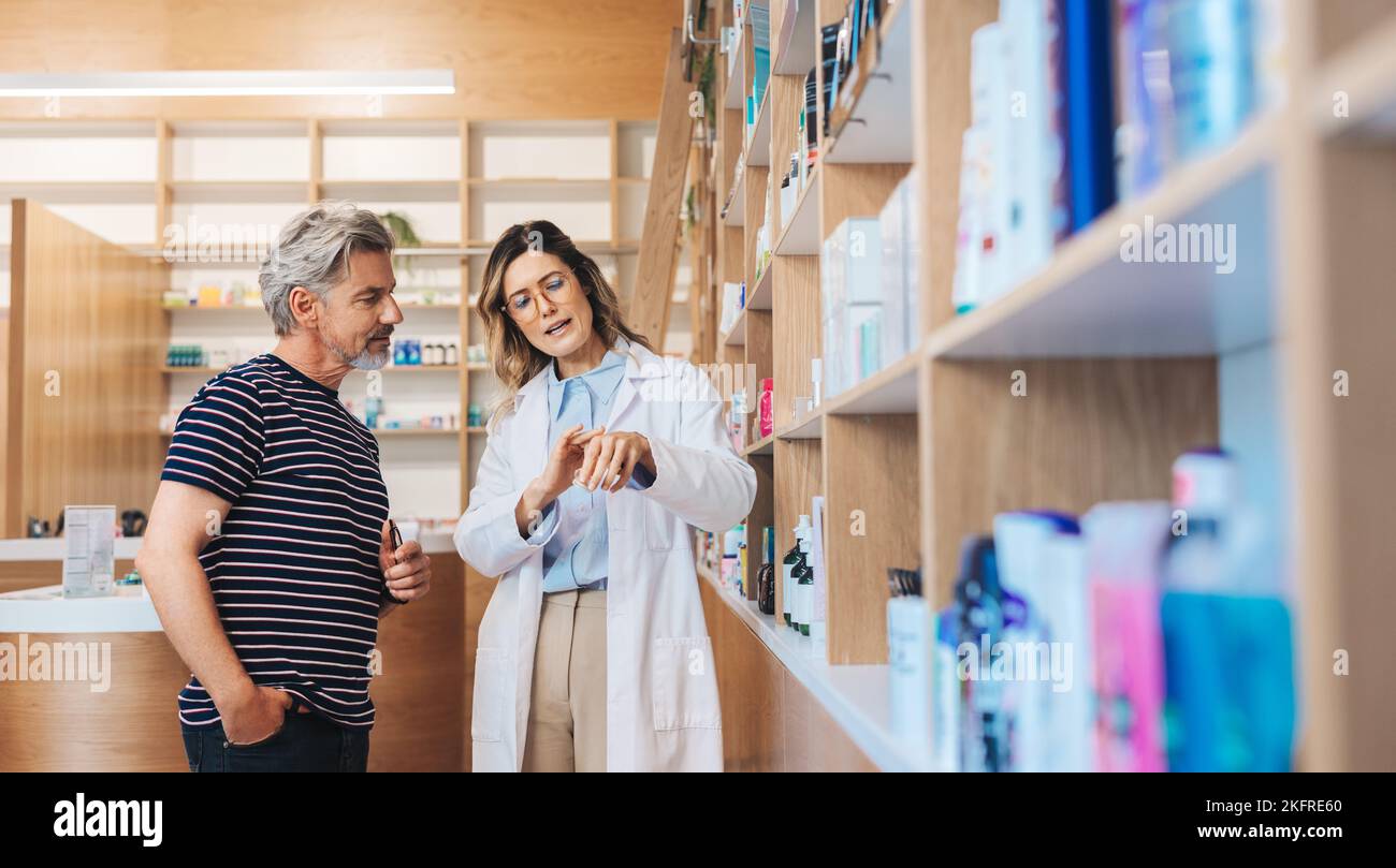 Female pharmacist assisting a man in a drug store. Healthcare professional showing a skincare product to a patient in a pharmacy. Stock Photo