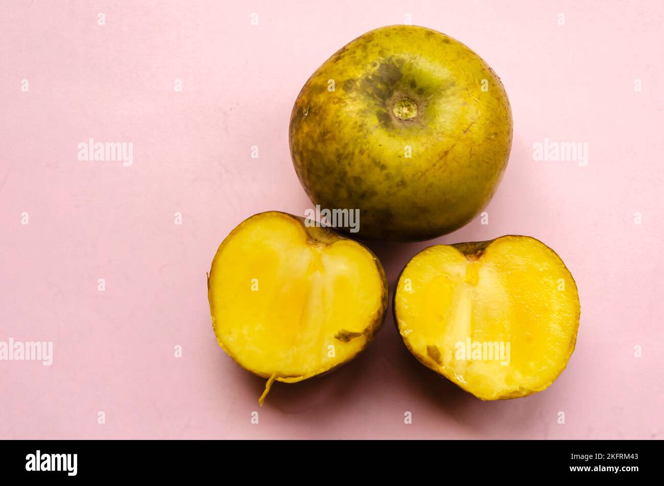 A whole and two halves ripe white sapote fruits are on a pink surface. Stock Photo