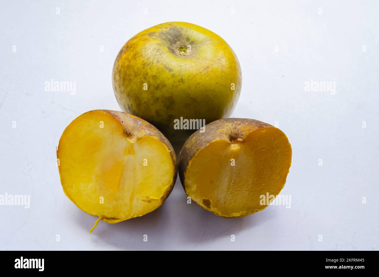 A whole and two halves ripe white sapote fruits are on a white surface. Stock Photo