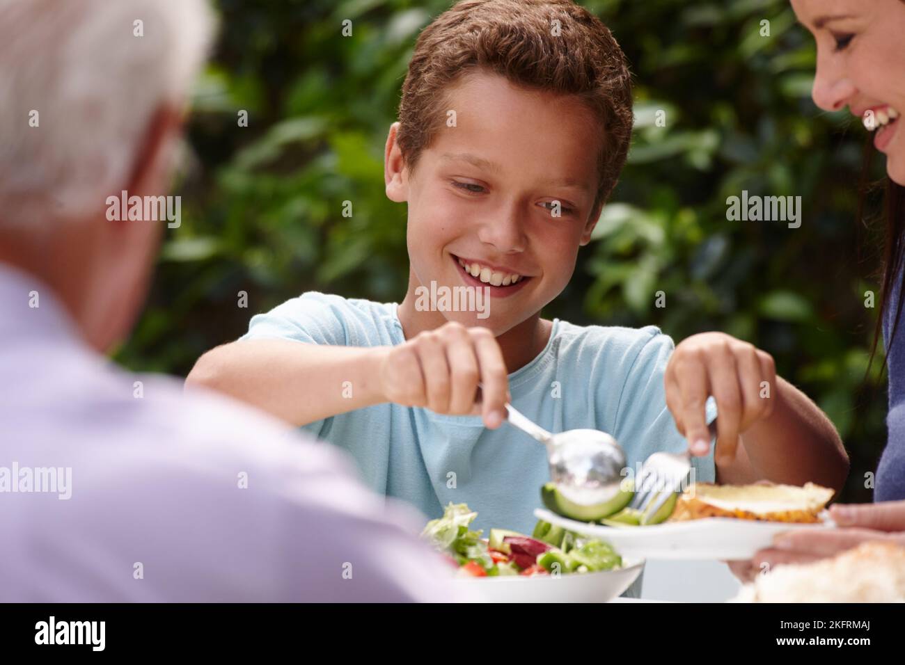 Tucking into some salad. a little boy having lunch with his family outside. Stock Photo