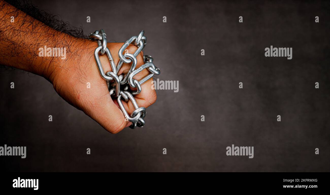 A metal chain is wrapped around a fist on a dark cement blurred background with copy space Stock Photo