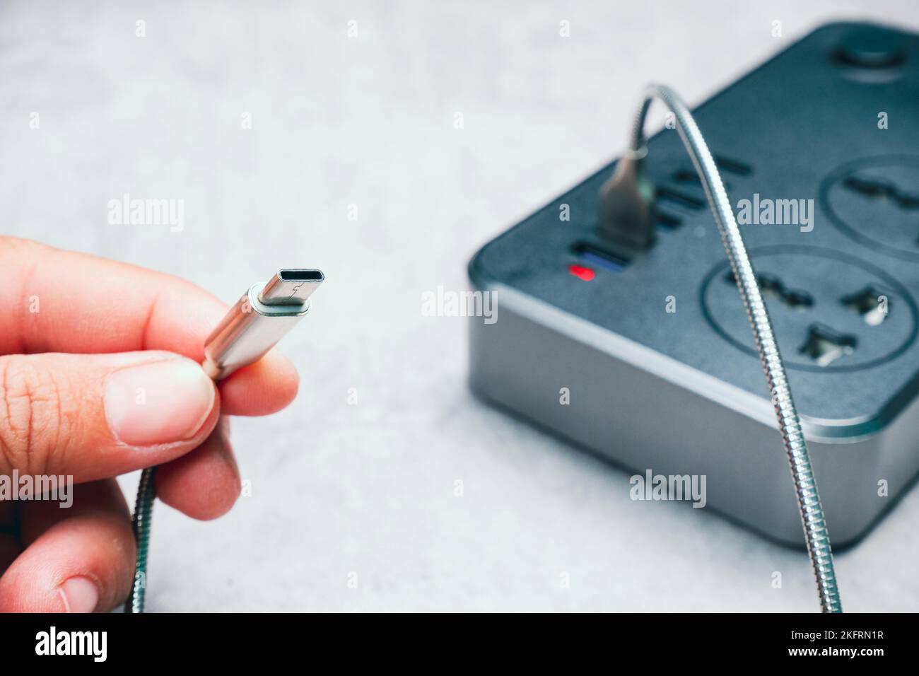 Human hand holding a type C mobile phone charger cable connected to a