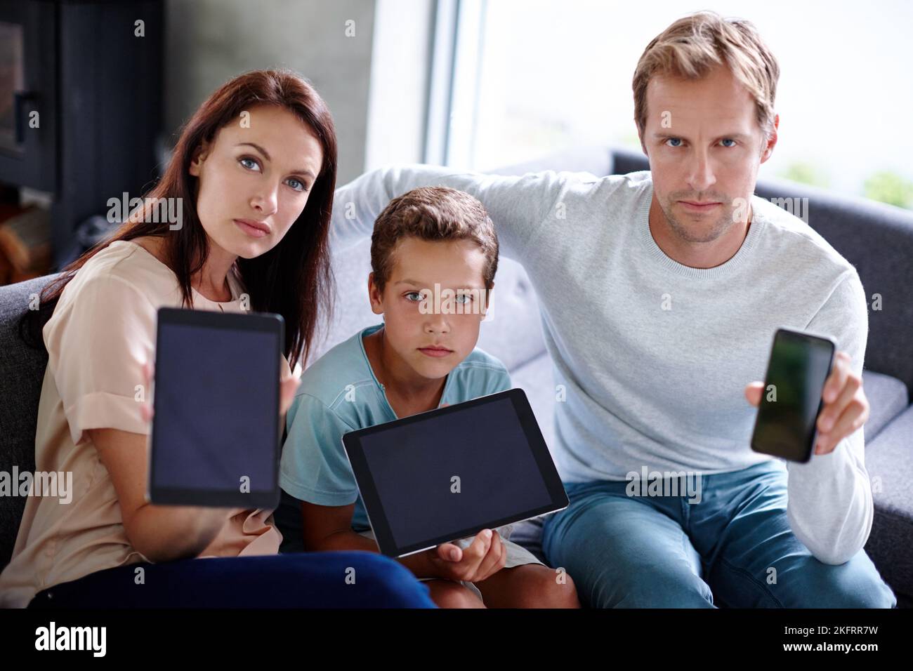 Technology is coming in the way of family time. Portrait of a family looking serious as they hold up their digital devices. Stock Photo