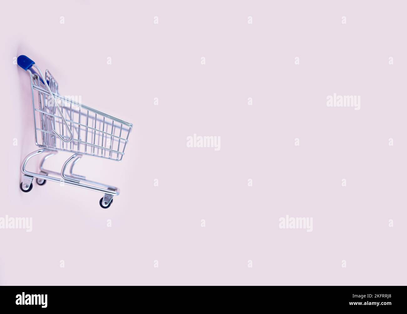 empty shopping cart over light pink background, mini metal cart isolated on color background Stock Photo