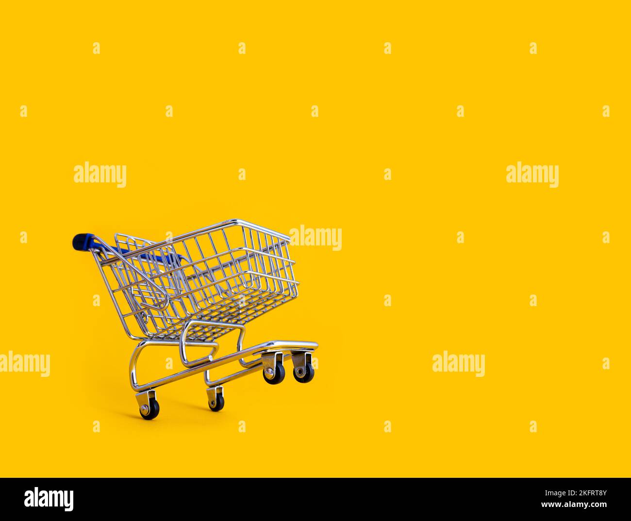 empty shopping cart over yellow background, mini metal cart isolated on color background Stock Photo