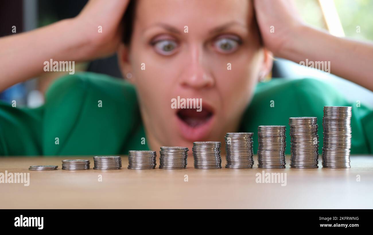 Shocked and surprised woman looks at stacks of coins on table. Stock Photo