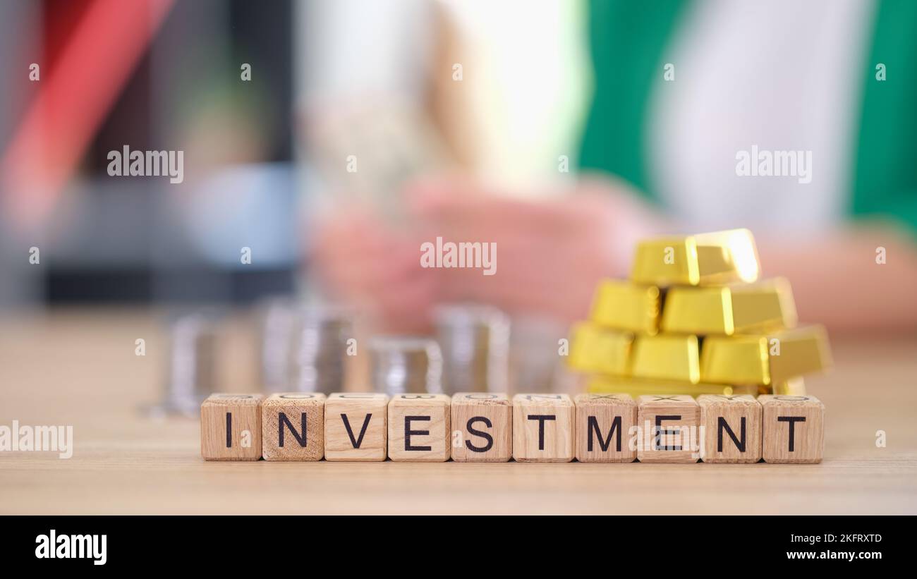 Word investment with gold bars and stacks of coins on table. Stock Photo