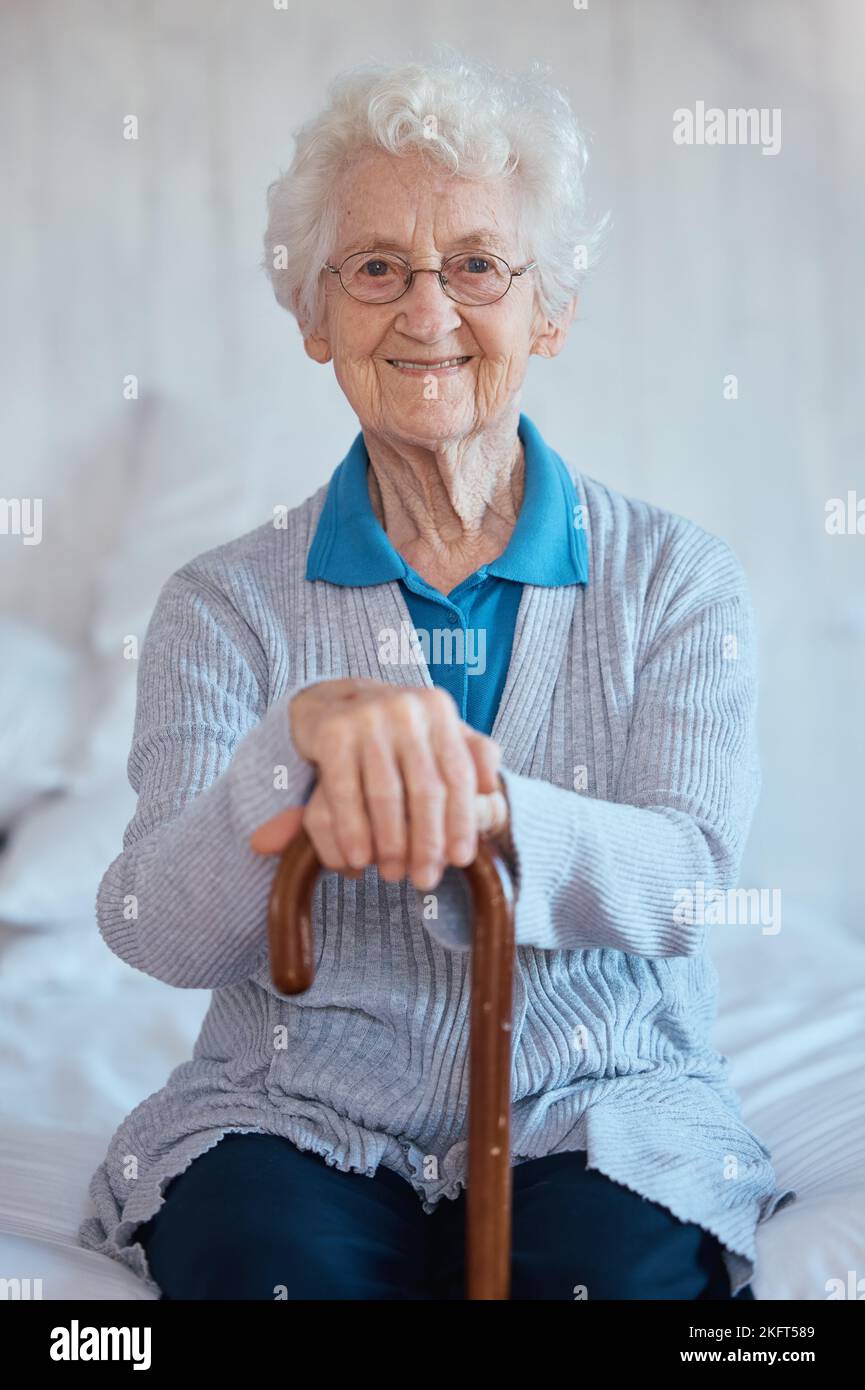 Elderly woman, sitting portrait and smile on bed with happiness, walking stick and relax in nursing home. Happy senior lady, bedroom and cane for Stock Photo