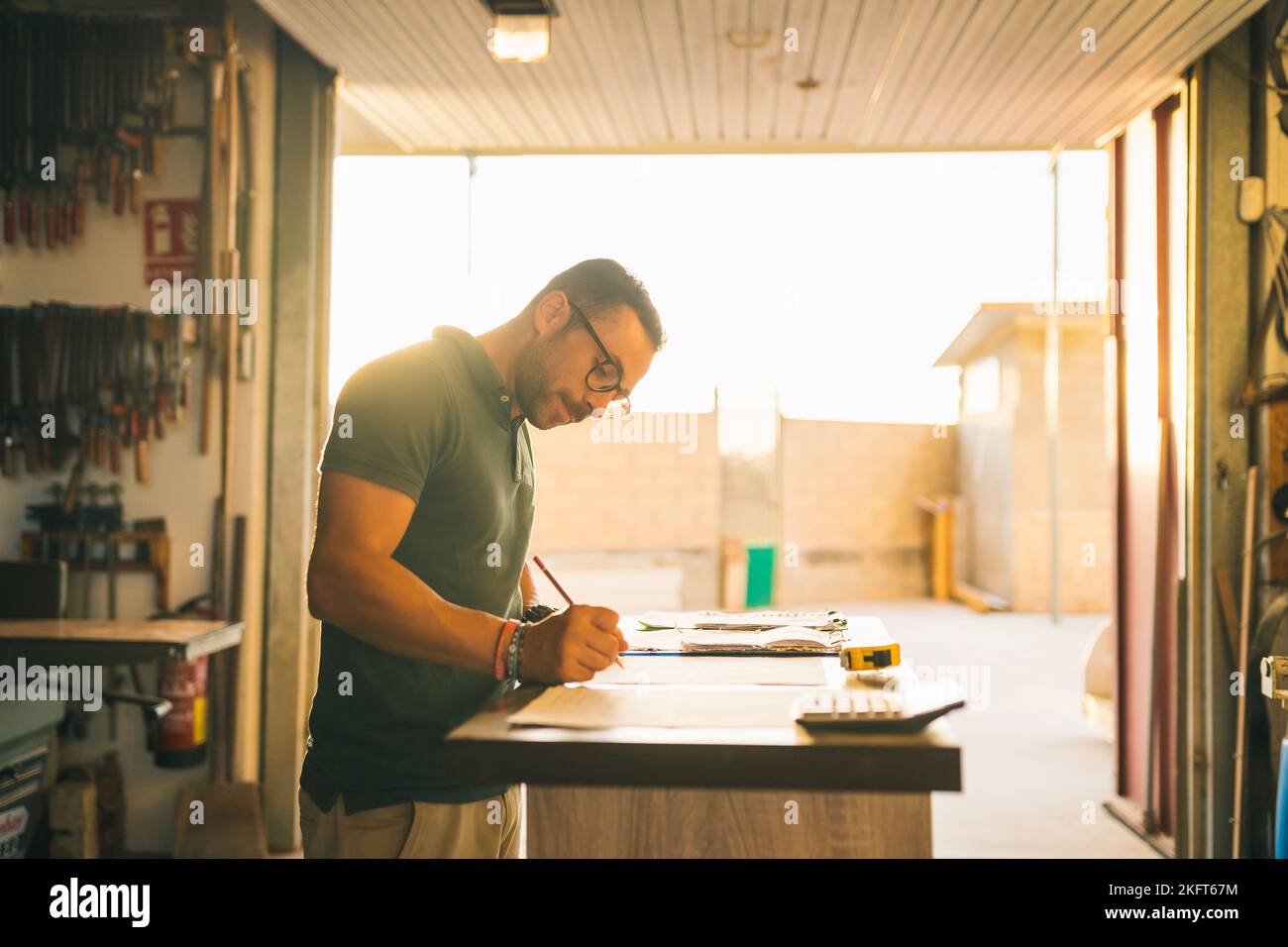 Concentrated male artisan writing on paper sheet while ordering parts at table in workshop Stock Photo
