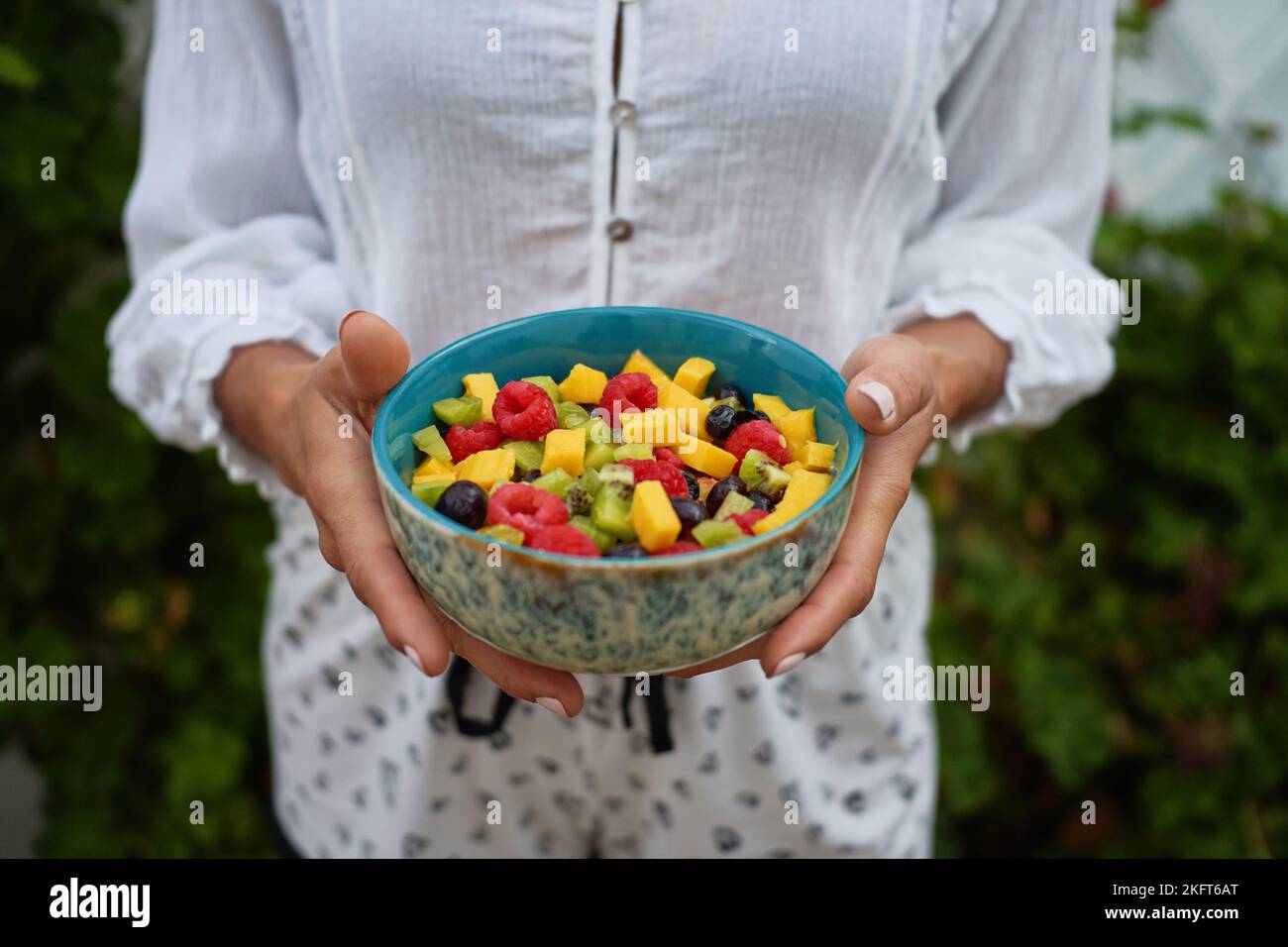 From above soft focus of anonymous female demonstrating bowl of healthy fruit salad on summer day in yard Stock Photo
