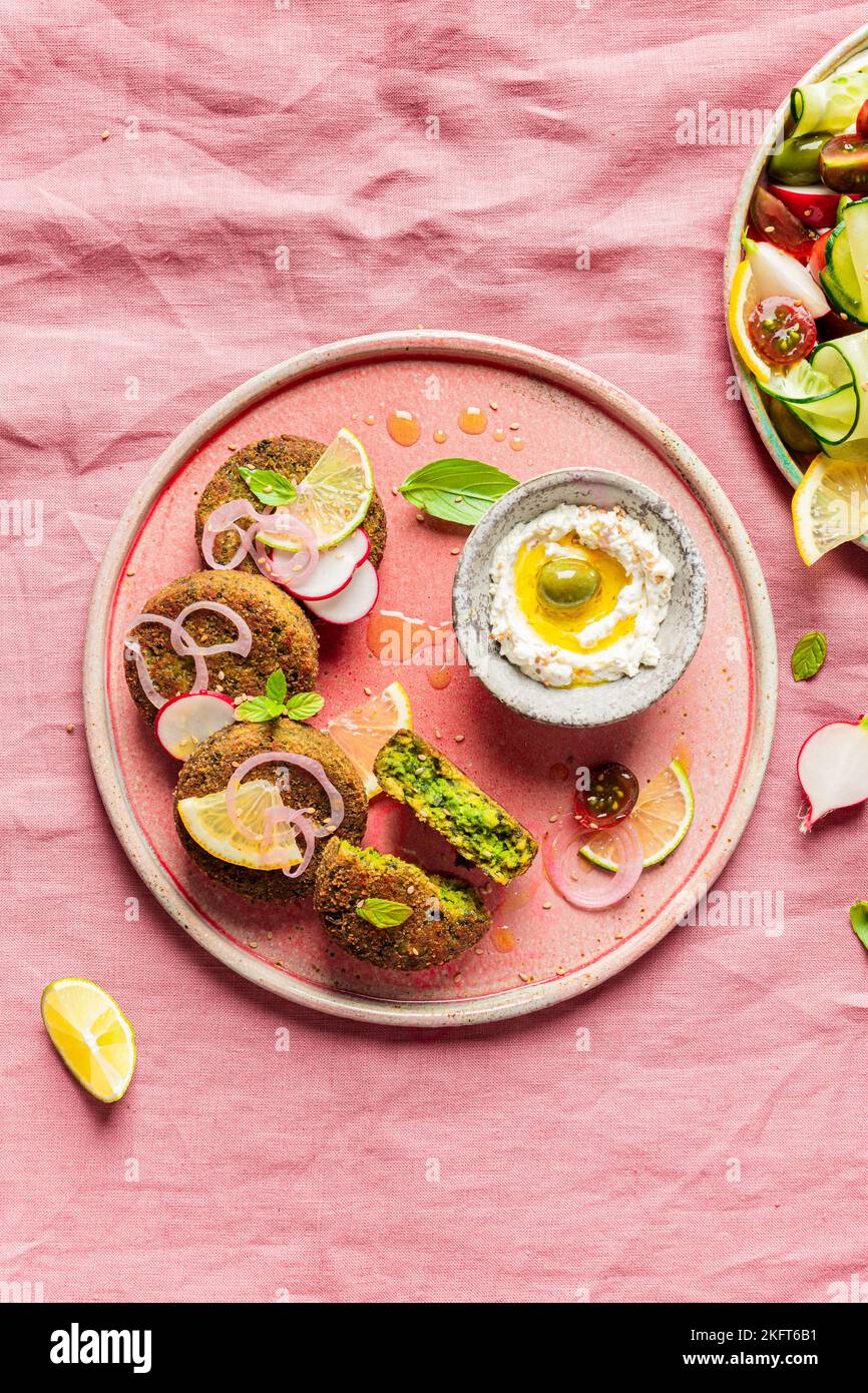 Top view of plate with delicious cream cheese and assorted vegetables placed on napkin near vegan fritters on pink background Stock Photo