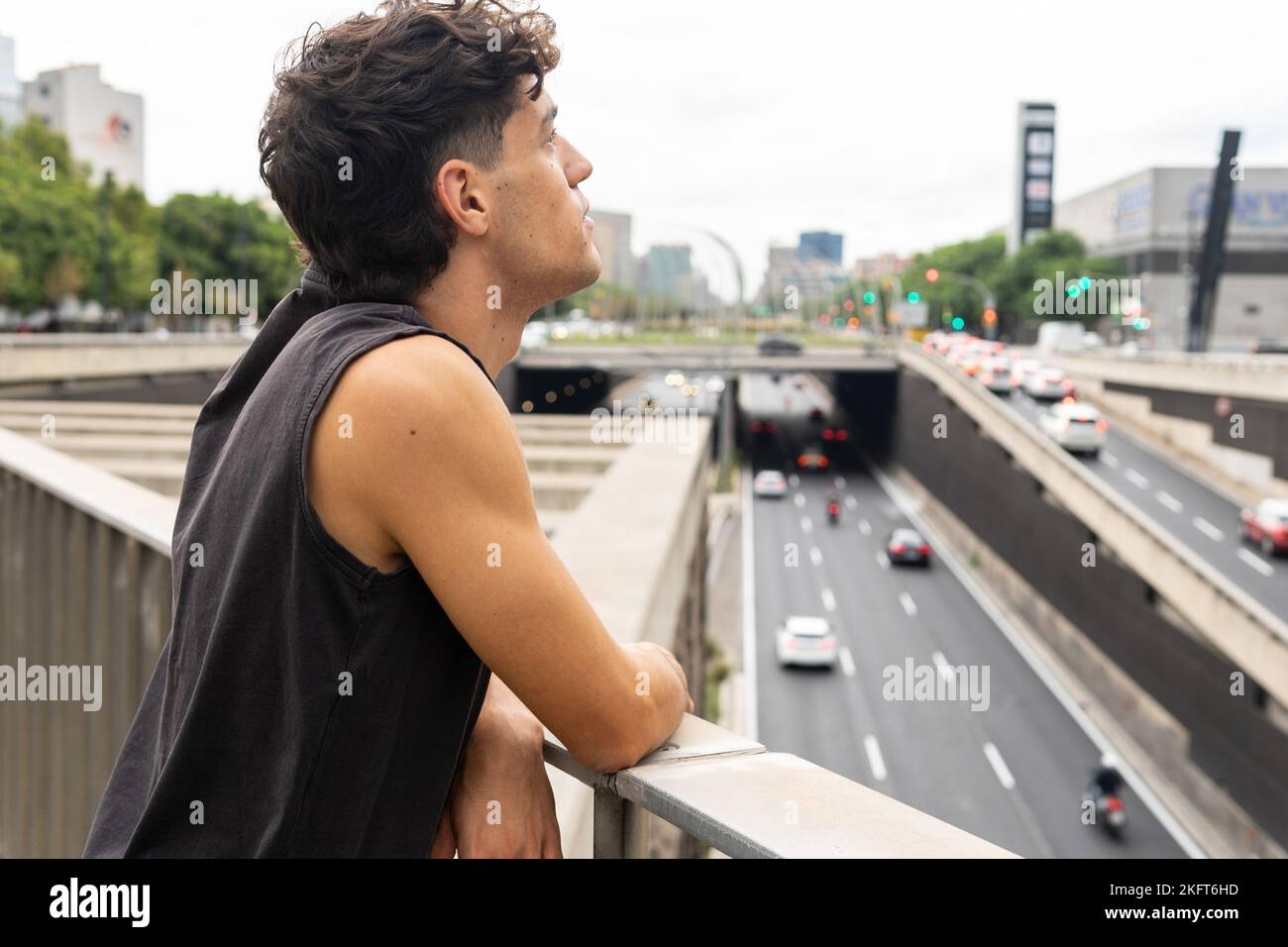 Young male in black tank top leaning on footbridge railing and ...