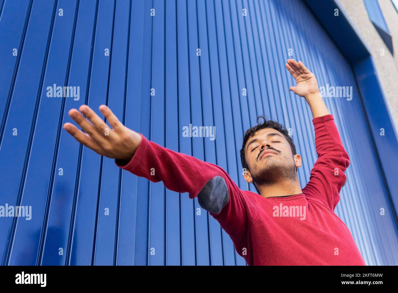 Low angle of male dancer in red sweatshirt performing movement with one hand raised and other outstretched Stock Photo