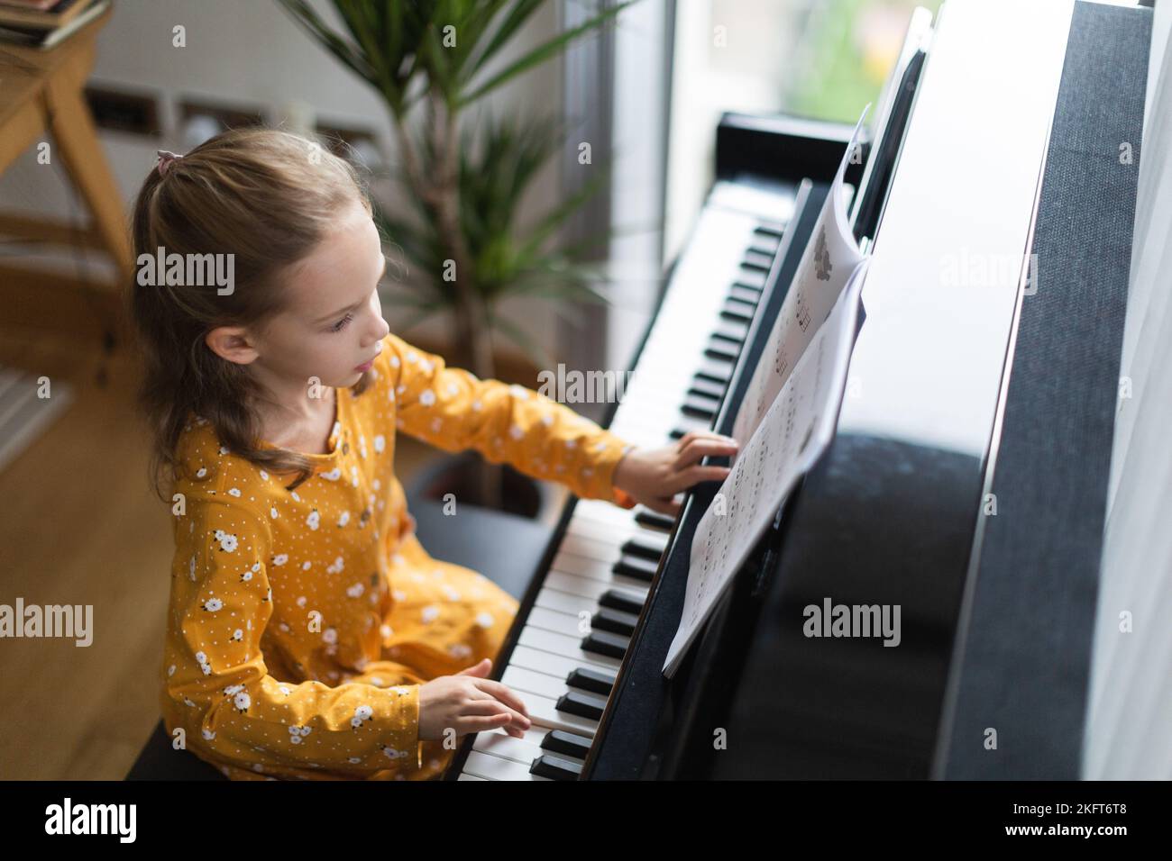 From above blonde little girl practicing music on piano in bright house interior Stock Photo