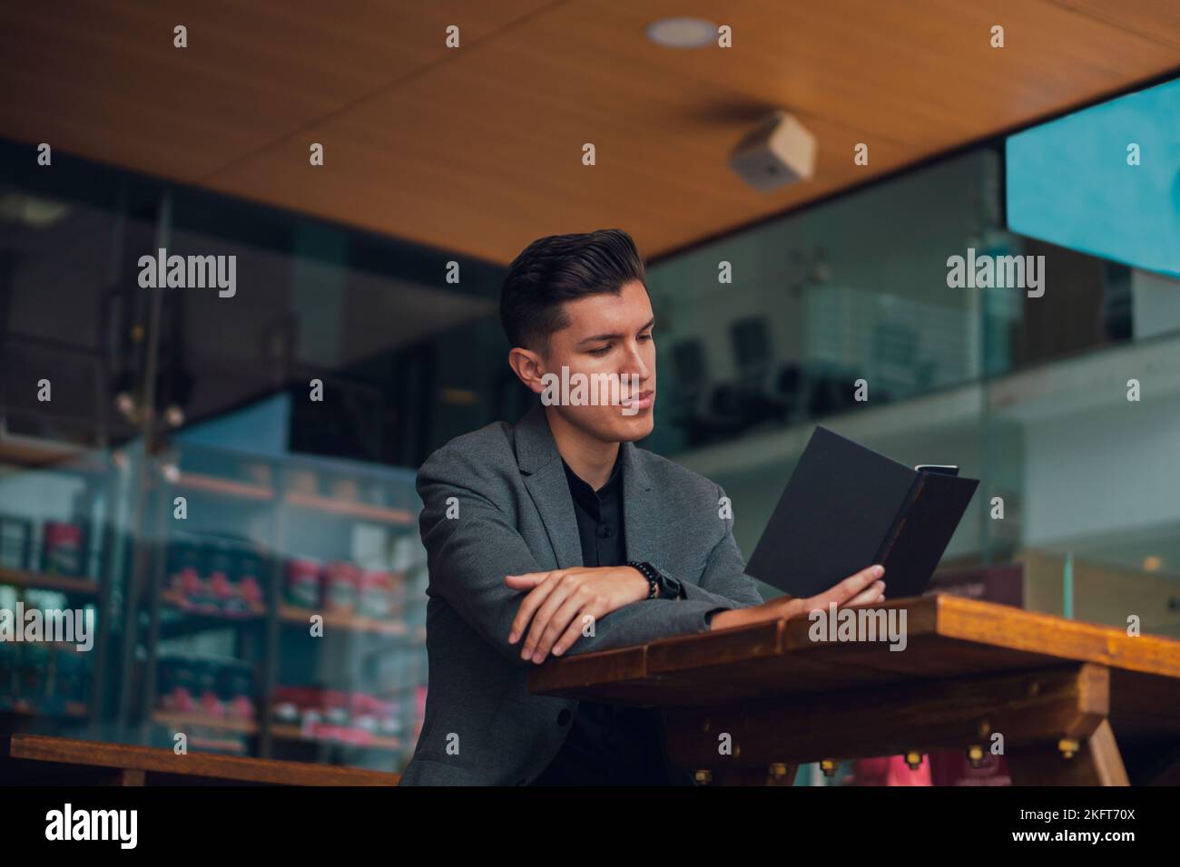 Concentrated young man in formal outfit sitting at table in cafeteria while reading notes in planner Stock Photo