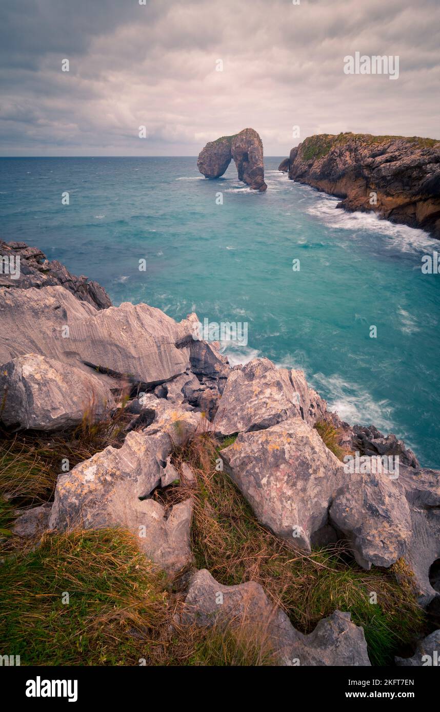 Spectacular scenery of rough rocky cliffs and formations placed in calm sea under bright cloudy sky in Asturias Stock Photo