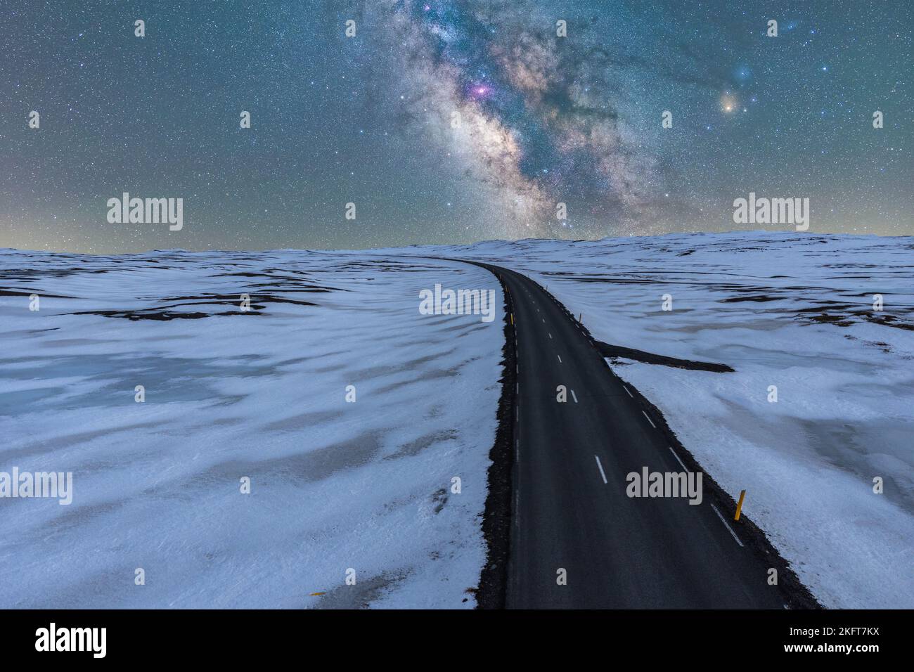Drone view of endless narrow road going between frozen land under sparkling sky with galaxy Stock Photo