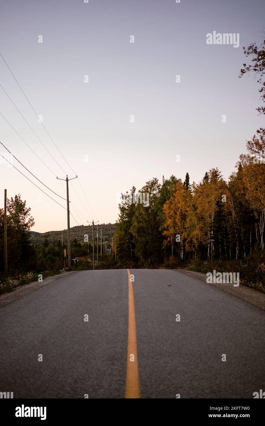 Paved road with yellow line leading to autumn trees in Canada woods under blue cloudless sunset sky Stock Photo