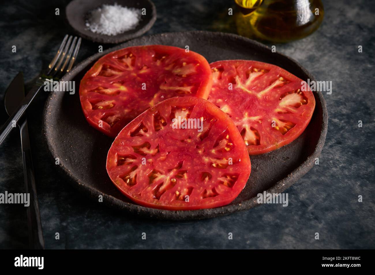 Delicious sliced tomatoes in cast iron plate near sea salt and jug of