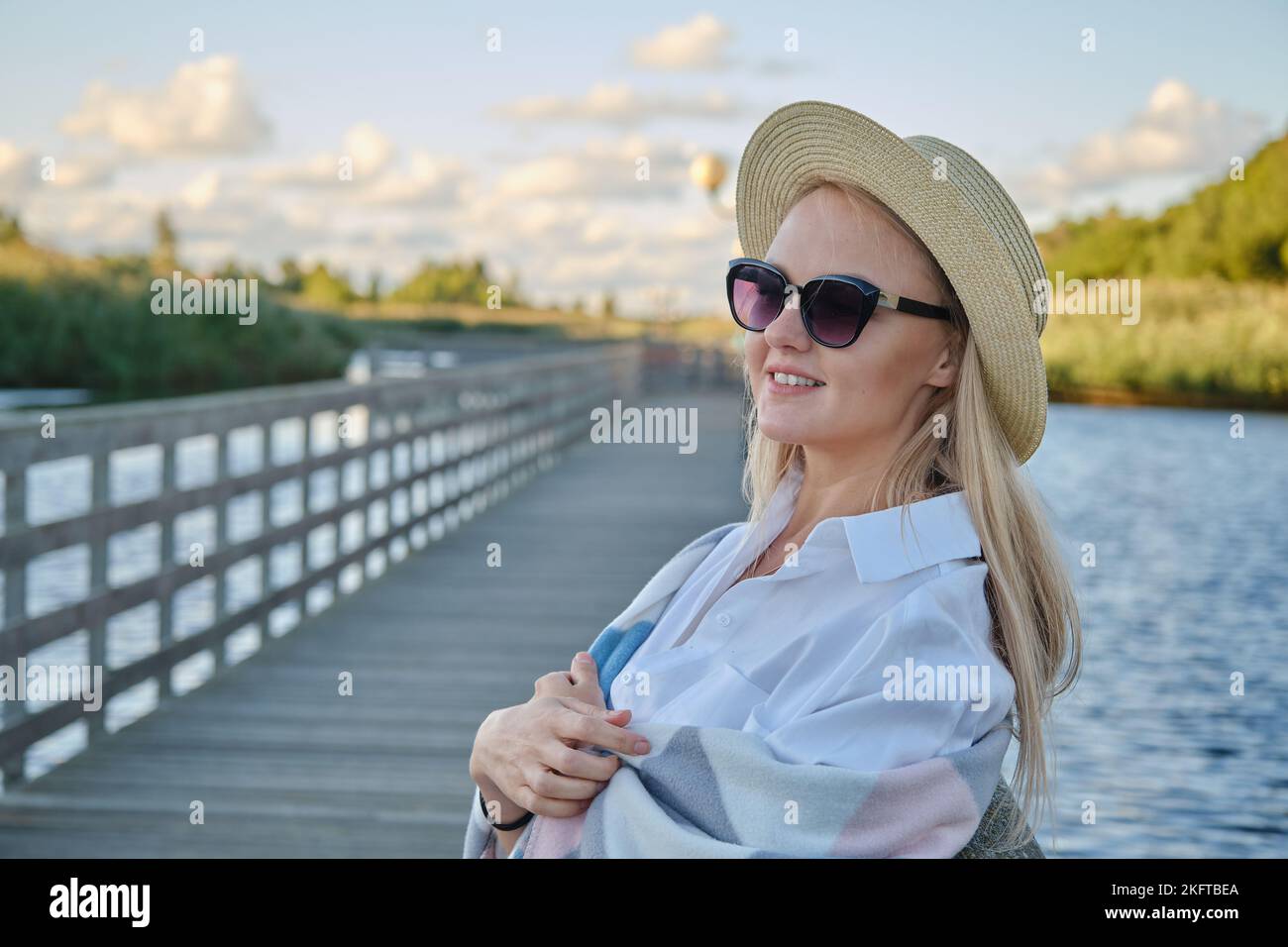young happy blond woman in straw hat and sunglasses at summer sunset ...