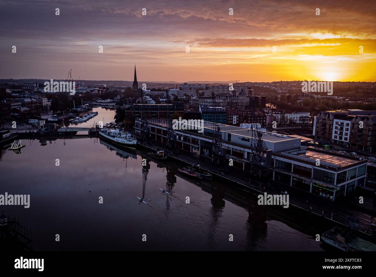 The sun rises over Bristol Harbourside as rowers cross the basin past the old docks on a cold, but sunny morning across the south west. Picture date: Sunday November 20, 2022. Stock Photo